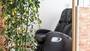A massage chair in a room with a brick wall and a potted plant. - Asaka Daily Hotel (Asaka)