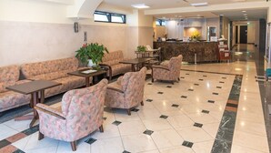 A hotel lobby with a reception desk, seating area with sofas and armchairs, and a tiled floor. - Asaka Daily Hotel (Asaka)