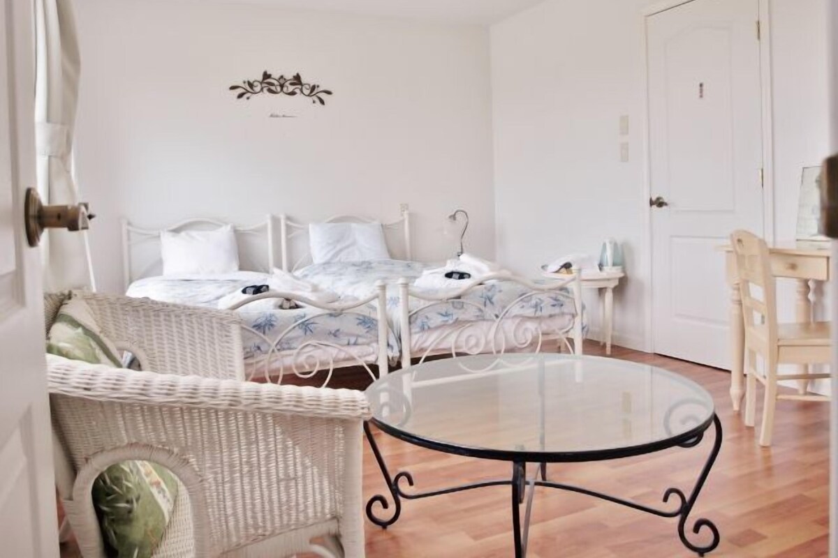 Un dormitorio con una cama, una silla de mimbre, una mesa de vidrio y una puerta.