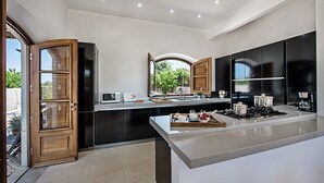 A modern kitchen with a large island, black cabinets, and a window overlooking a garden. - Beautiful Charming villa with pool, near Fabrica Beach in Cacela Velha. (Vila Nova de Cacela)