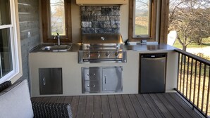 An outdoor kitchen with a stone backsplash, stainless steel appliances, and a view of the outdoors.