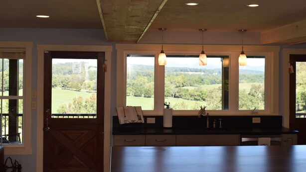 A kitchen with large windows, wooden ceiling, and pendant lights.