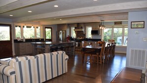 A spacious kitchen with a dining area, wooden flooring, and large windows.