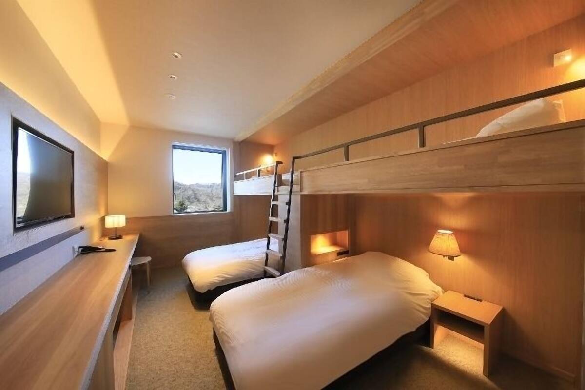 A compact hotel room with bunk beds, a TV, bedside lamps, and a window.