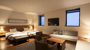A hotel room with two beds, a sofa, a small table, and two chairs. There are two windows with curtains, a wall-mounted TV, and a headboard with a light fixture. - Takamine Mountain Hotel (Tsumagoi)
