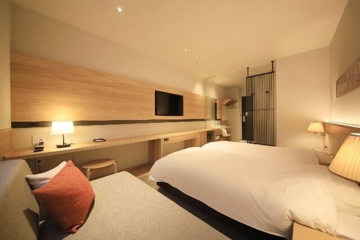 A hotel room with a bed, a desk, a chair, a TV, and a lamp.