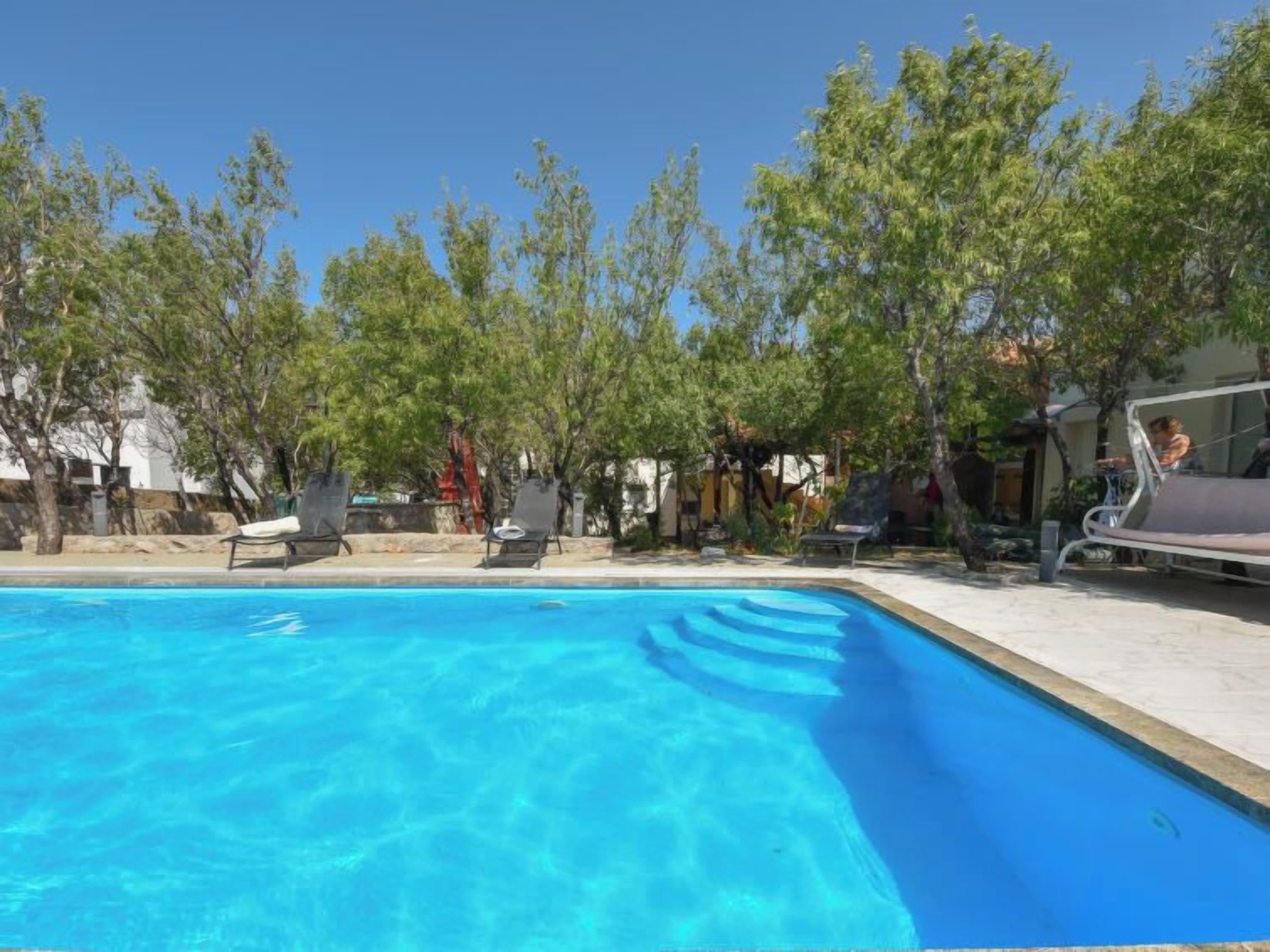 A swimming pool with clear blue water, surrounded by trees and lounge chairs.