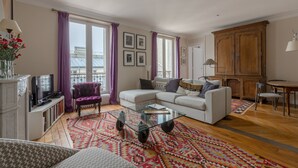A living room with a white sofa, a glass coffee table, a purple armchair, and a dining area with a wooden cabinet.
