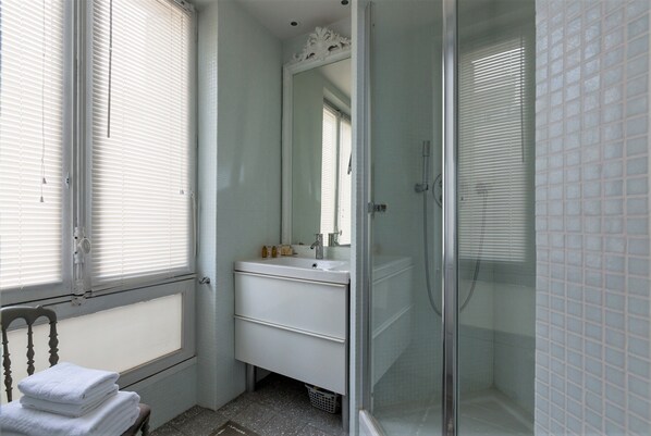 A bathroom with a white sink, mirror, and shower. - Creative Paradise in Bastille, by Veeve (Paris)