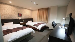 Una habitación de hotel con dos camas, un escritorio con computadora, una silla, teléfono y televisor montado en la pared.