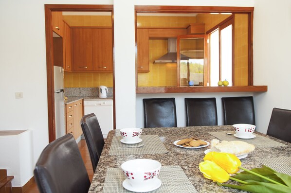 A dining area with a table set for four, including white cups with red floral patterns, a plate of cookies, and a loaf of bread. - Villa with 3 bedrooms, private pool, walking distance to the beach. (Cala D' Or)