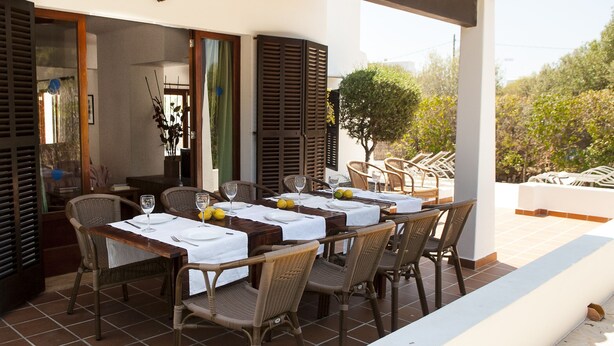 An outdoor dining area with wicker chairs and tables set up on a terrace, overlooking a garden and trees. - Villa with 3 bedrooms, private pool, walking distance to the beach. (Cala D' Or)