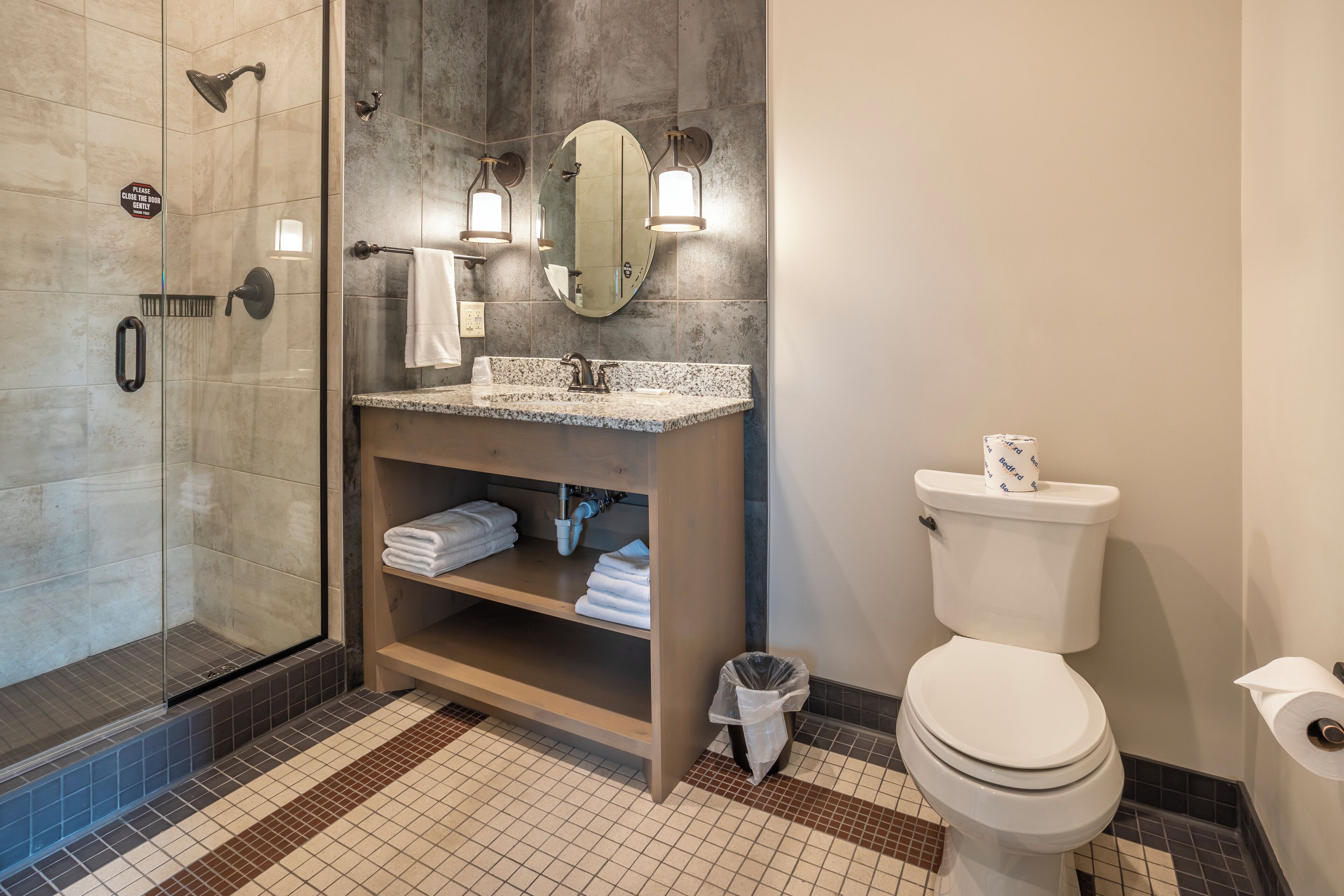 A bathroom with a shower, a toilet, a sink with a mirror, and a towel rack.