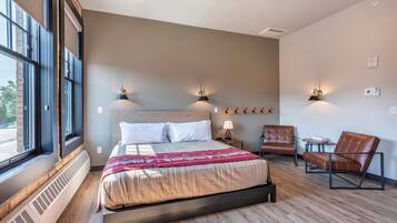 Une chambre d’hôtel moderne avec un grand lit, deux lampes fixées au mur, une chaise et une petite table.