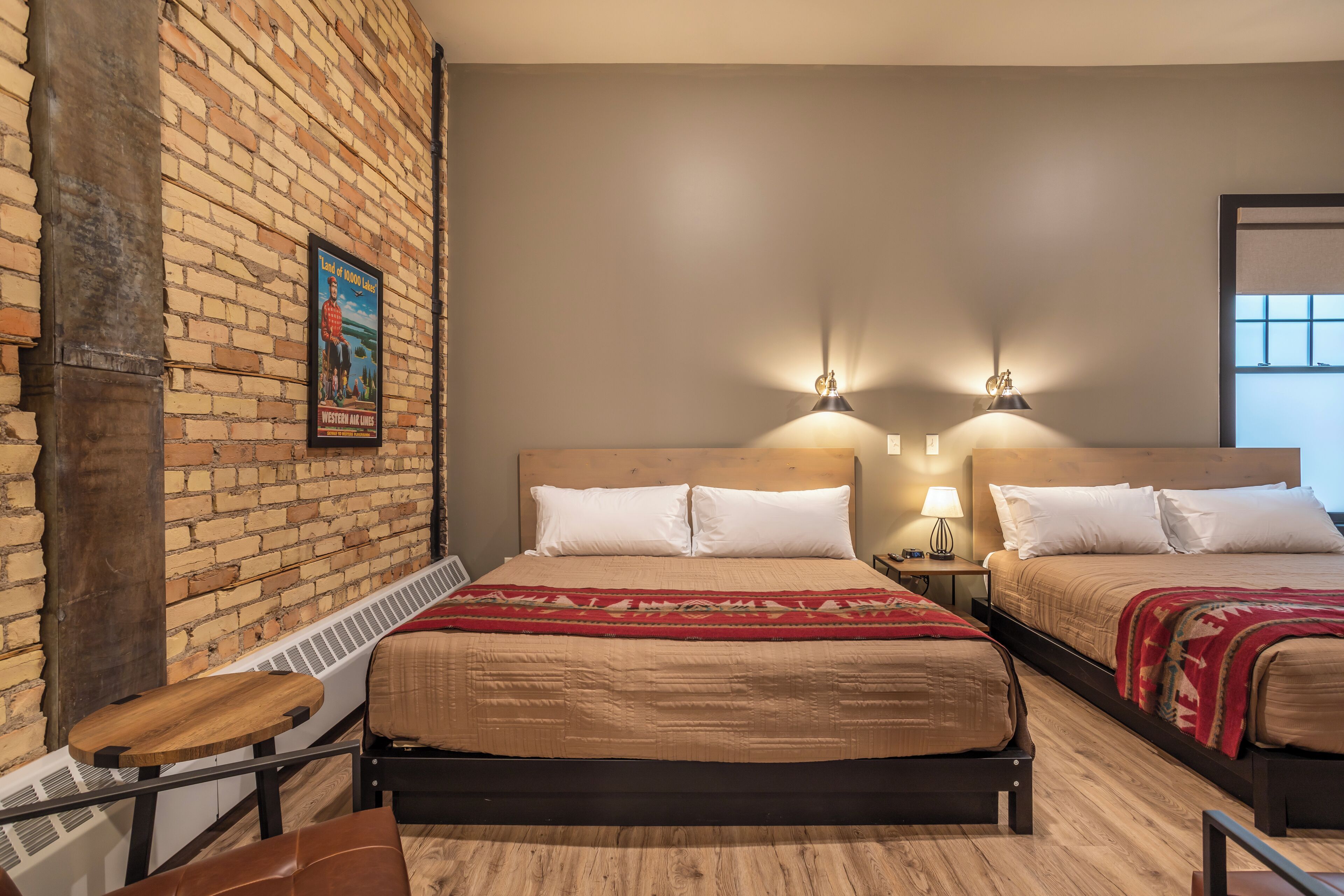 A hotel room with two beds, a brick wall, and a wooden floor.