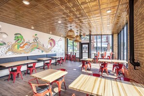 A restaurant interior with wooden tables and red chairs, a mural on the wall, and large windows. - Crosby Lofts (Crosby)