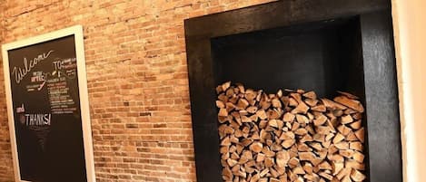 A brick wall with a blackboard displaying a welcome message and a fireplace with a stack of firewood.