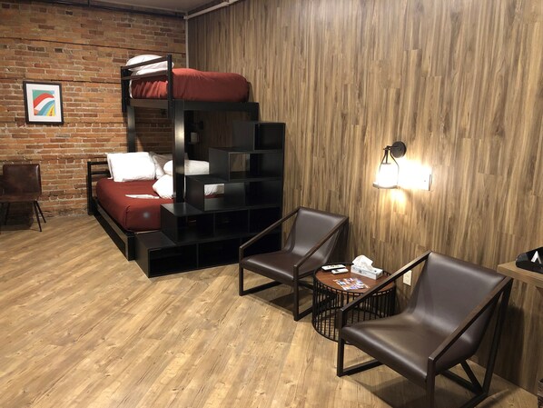 A room with a bunk bed, two chairs, a small table, and a wall-mounted lamp. - Crosby Lofts (Crosby)