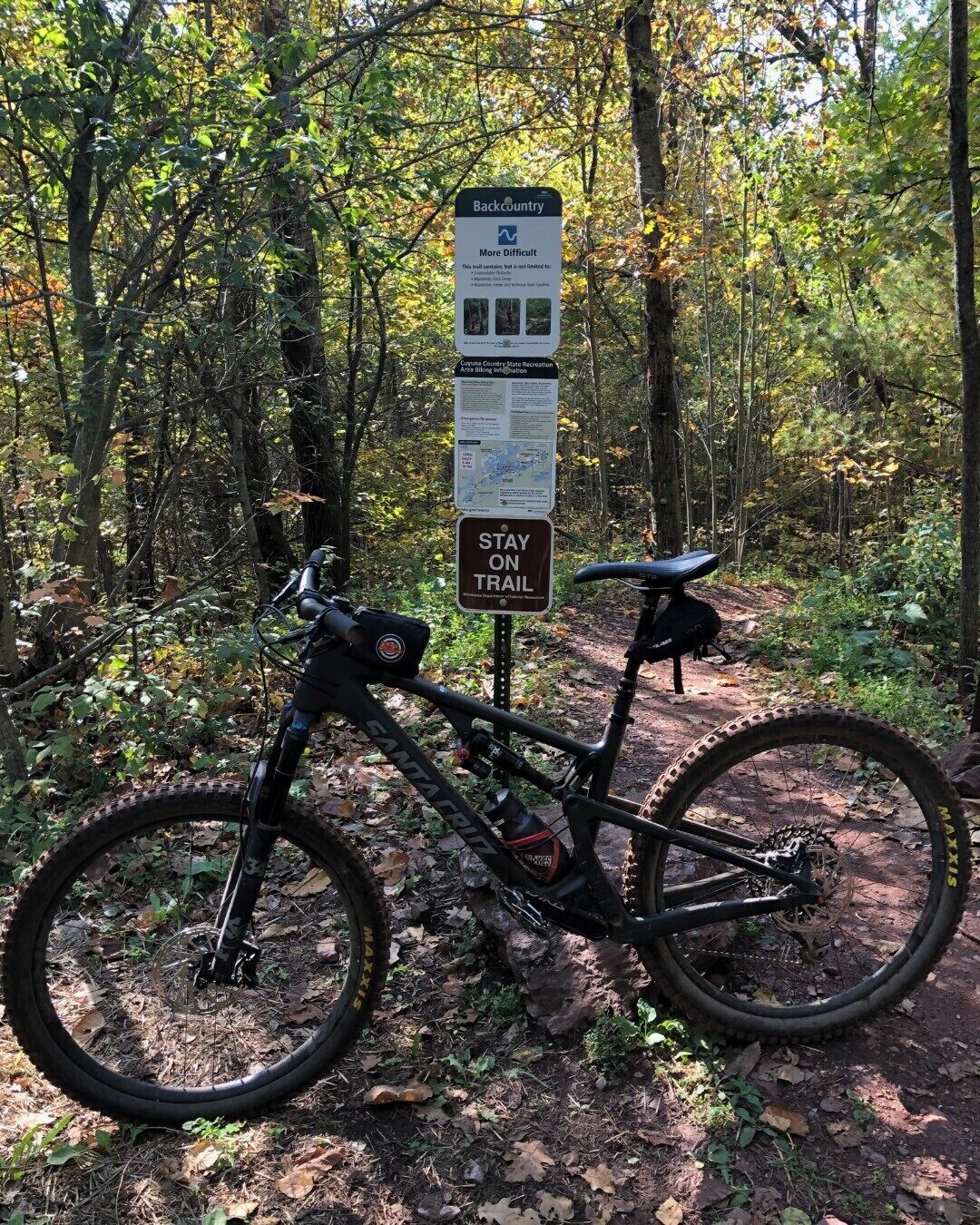 A mountain bike parked next to a trail sign in a forested area.