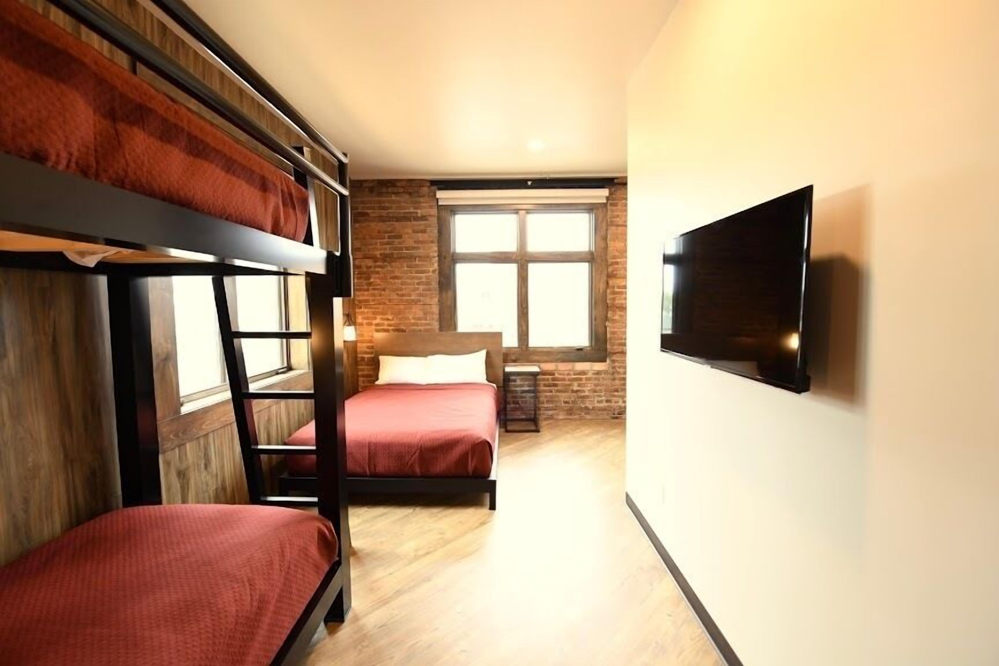 Un dormitorio con literas, un televisor, una pared de ladrillo y una ventana.