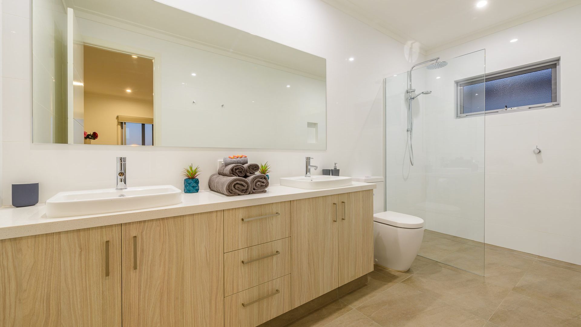 A modern bathroom with a large mirror, two sinks, a toilet, and a glass-enclosed shower.