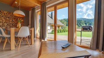 Un espace repas moderne avec une table en bois, des chaises et une vue sur un paysage montagneux grâce à de grandes fenêtres.