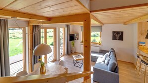 A spacious living area with a wooden ceiling, large windows, a grey sofa, and a dining table. - Chaty Pod Beskidkiem by Interhome (Szczyrk)