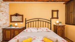 A bed with floral bedding, two bedside tables with lamps, a wooden headboard, a stone wall, and a wooden wardrobe. - Authentic Istrian House - Apartment with saltwater pool- 15 min from Kamenjak (Pula)