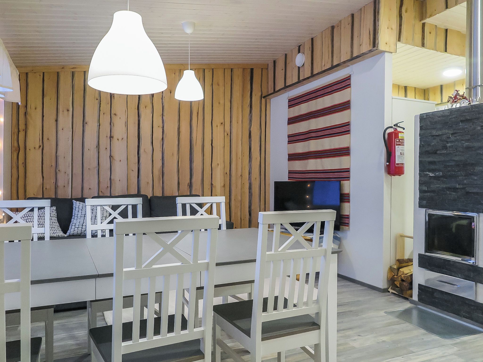 Una habitación con pared de madera, un sofá blanco, una televisión y una chimenea.