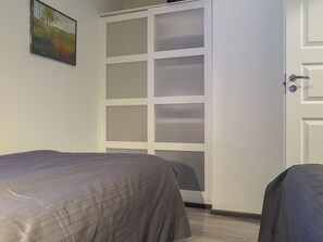 Une chambre avec deux lits, une porte blanche dotée de panneaux en verre dépoli et un tableau accroché au mur.