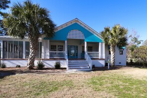 A two-story house with a blue roof and white exterior, a front porch with steps, and a small garden area. - Home with golf cart,community pool,Spinnakers Reach community (Emerald Isle)