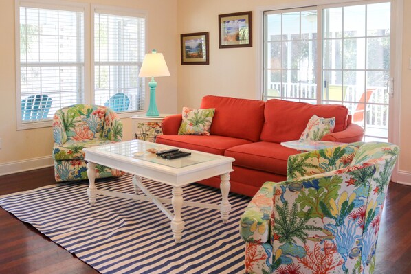 A living room with a red sofa, two floral armchairs, a glass coffee table, and a striped rug. - Home with golf cart,community pool,Spinnakers Reach community (Emerald Isle)