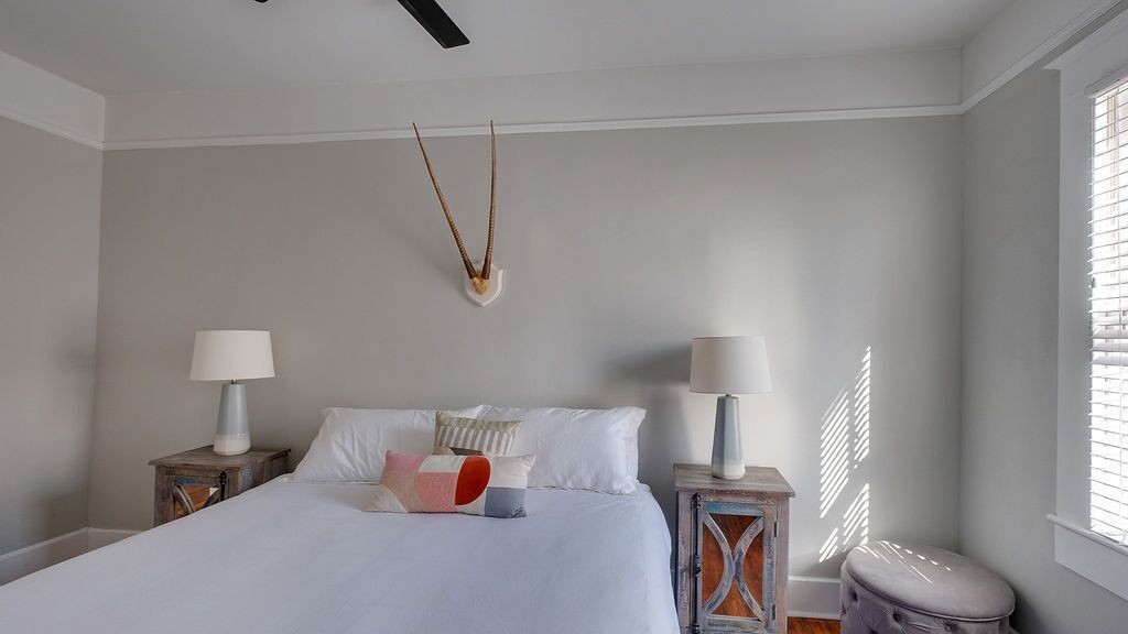 A bedroom with a bed, two bedside tables with lamps, a wall-mounted decor, and a window with blinds.