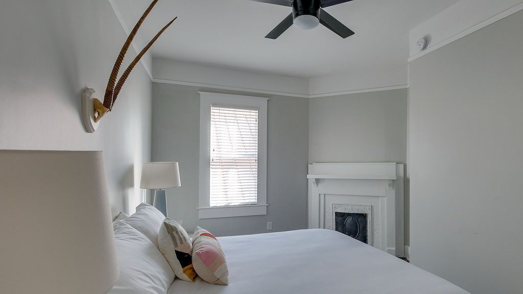 A bedroom with a bed, a ceiling fan, a fireplace, and a window with blinds.