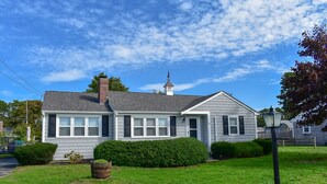 A two-story house with a chimney, a small tower-like structure on the roof, and a well-maintained lawn.
