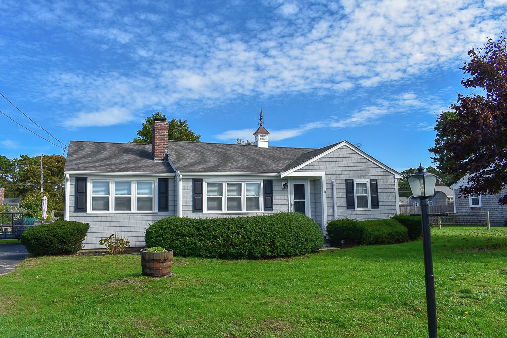 A two-story house with a chimney, a small tower-like structure on the roof, and a well-maintained lawn.