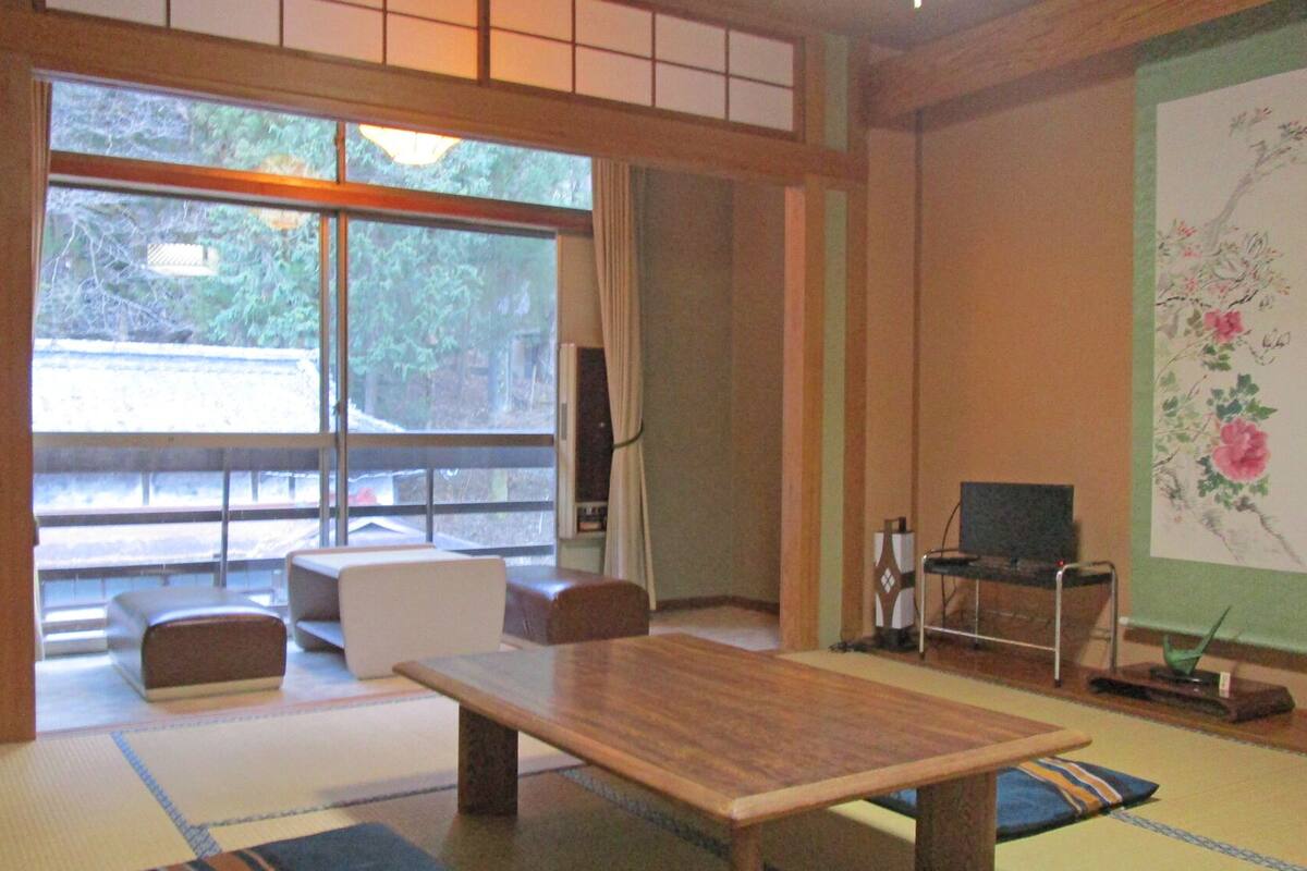 Une pièce de style japonais traditionnel, avec un sol recouvert de tatamis, une table basse, un canapé et un téléviseur.