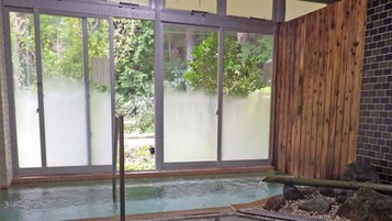 Un área de aguas termales con un muro de madera, piso de baldosas y un separador de vidrio.