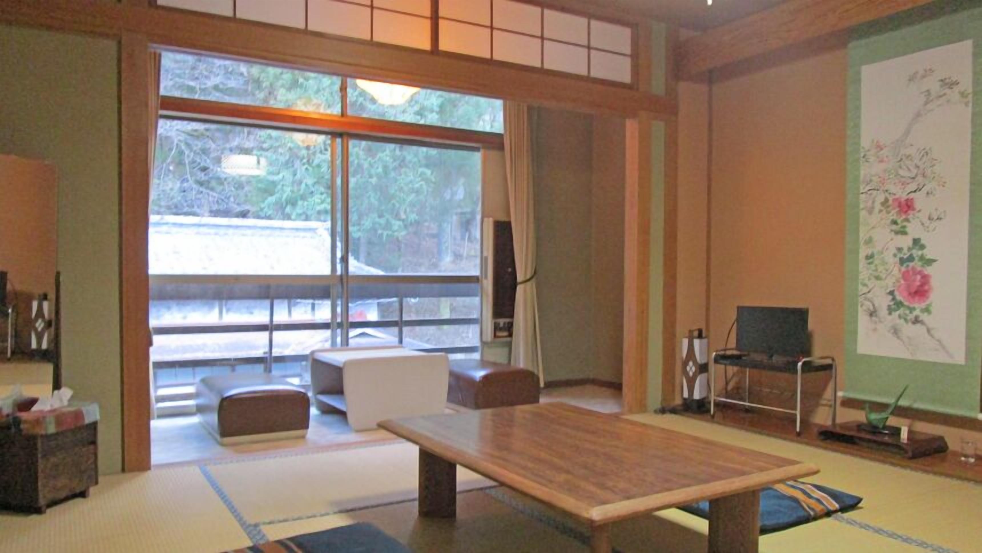 A traditional Japanese room with tatami flooring, a low table, a sofa, and a television.