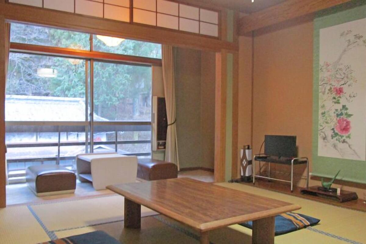 Une pièce de style japonais traditionnel, avec un sol recouvert de tatamis, une table basse, un canapé et un téléviseur.
