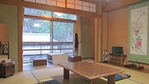 A traditional Japanese room with tatami flooring, a low table, a sofa, and a television. - Nakaya Ryokan (Ueda)