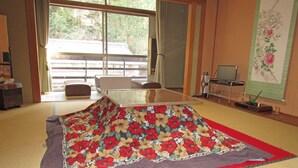 A tatami mat room with a low table, a TV, and a decorative wall hanging. - Nakaya Ryokan (Ueda)