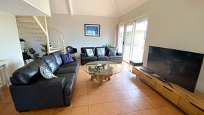 A living room with a black leather sofa, a glass coffee table, and a flat-screen TV on a wooden stand. - Osprey Holiday Village Unit 117 - Villa with a Pool in the Complex (EXMOUTH)