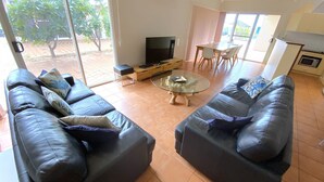 A living room with a sofa set, a coffee table, a TV, and a dining area with a table and chairs. - Osprey Holiday Village Unit 117 - Villa with a Pool in the Complex (EXMOUTH)
