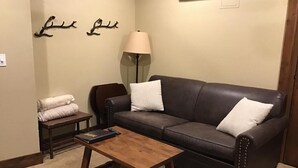 A living room with a dark brown leather sofa, two white pillows, a wooden coffee table, a small side table with a lamp, and wall art. - Upscale slope side resort in Breckenridge, CO (Breckenridge)