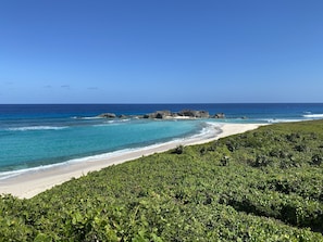 Een strand met helder turquoise water, een zandstrand en weelderige begroeiing op de voorgrond.