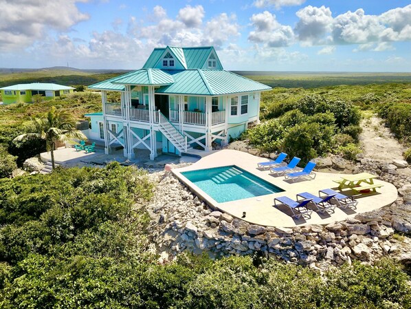 A turquoise house with a pool and lounge chairs.