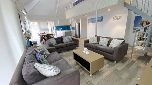A modern living room with two grey sofas, a coffee table, and a staircase. - Osprey Holiday Village Unit 121 - Villa with a Pool in the Complex (EXMOUTH)