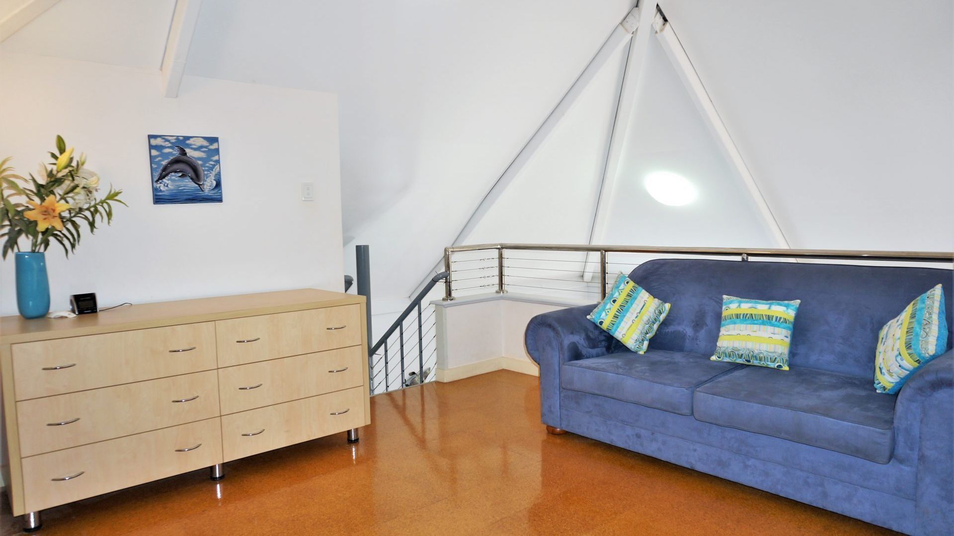 A room with a blue sofa, a wooden dresser, a painting of a dolphin, and a staircase.