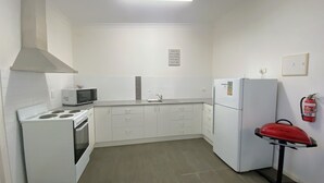 A compact kitchen with white appliances, a microwave, a stove, a sink, and a refrigerator. There is a fire extinguisher mounted on the wall.